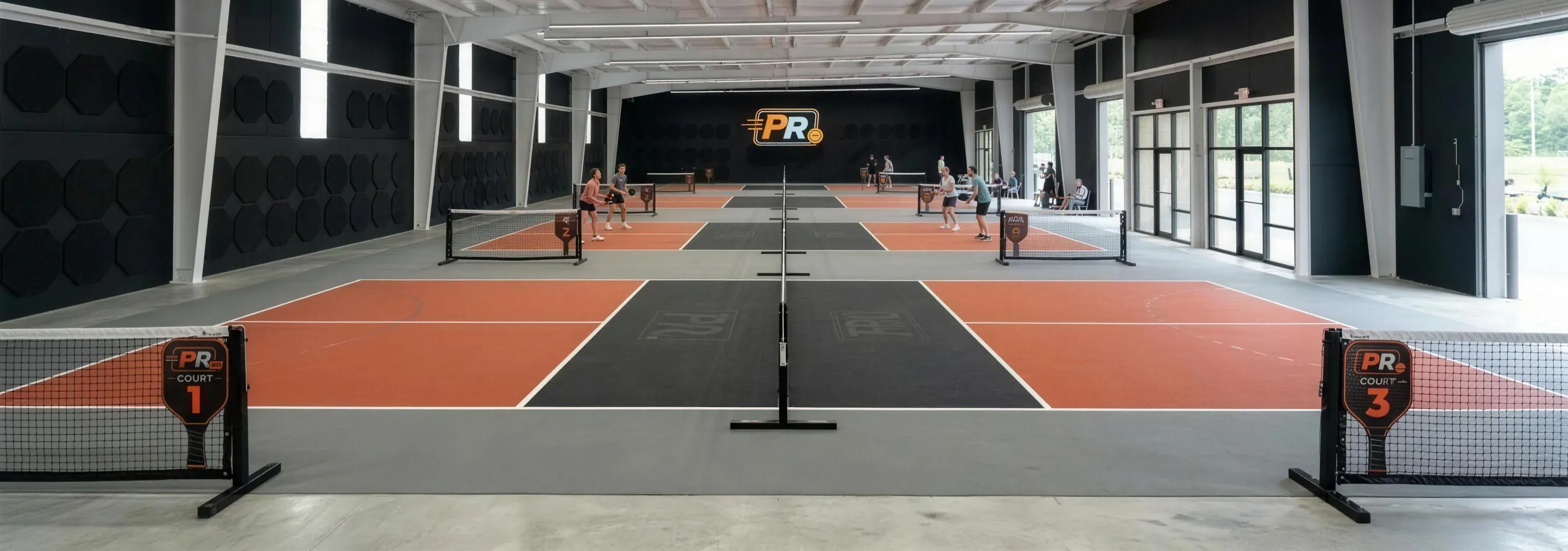 Players on the indoor courts at The Pickleball Reserve, with the PR sign on the back wall